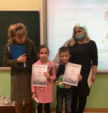 Pani Dyrektor po lewej stronie, w  środku stoi dziewczynka i chłopiec, którzy prezentują dyplomy, po prawej stronie stoi pani Bogusława 