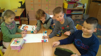 Czworo dzieci (jedna dziewczynka i troje chłopców) rysuje laurkę dla Ciszaków.